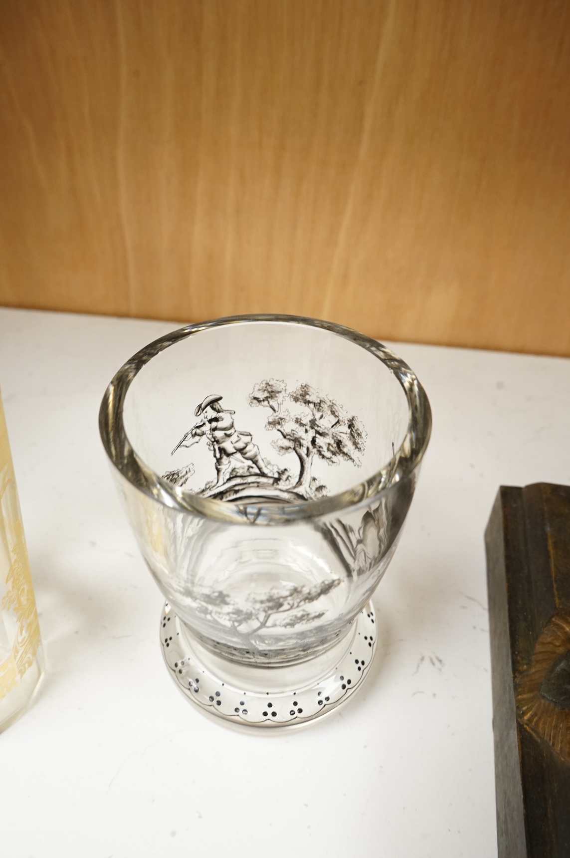 An Italian gilt-decorated and faceted beaker, inscribed Daniel Delvinis, the reverse with papal coat of arms, and a German Schwarzlot black enamelled ‘hunting’ beaker, largest 12cm (2)